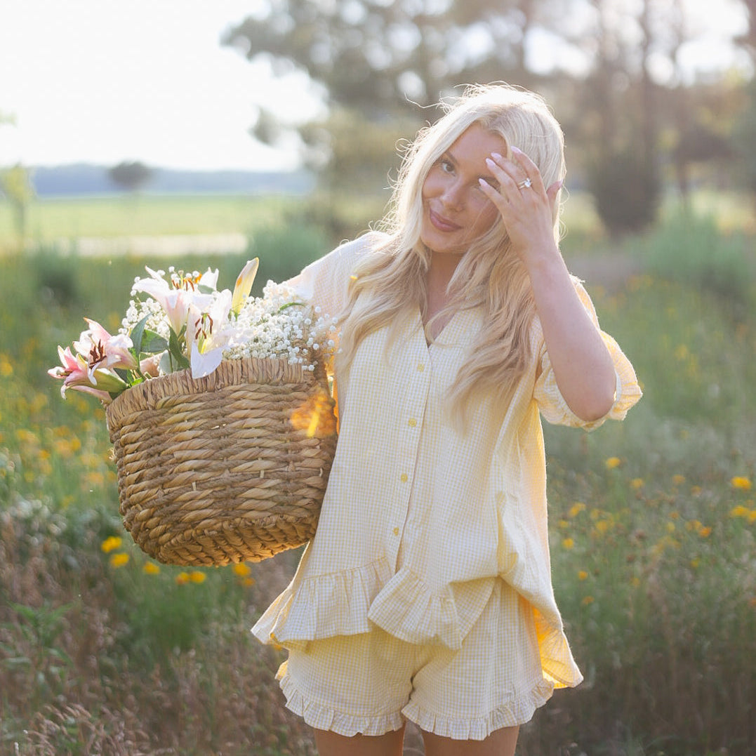 Woman in a yellow outfit holding a basket of flowers in a sunlit field.