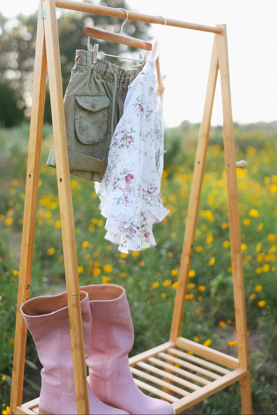 Wooden rack with shorts, a floral dress, and pink boots against a natural background
