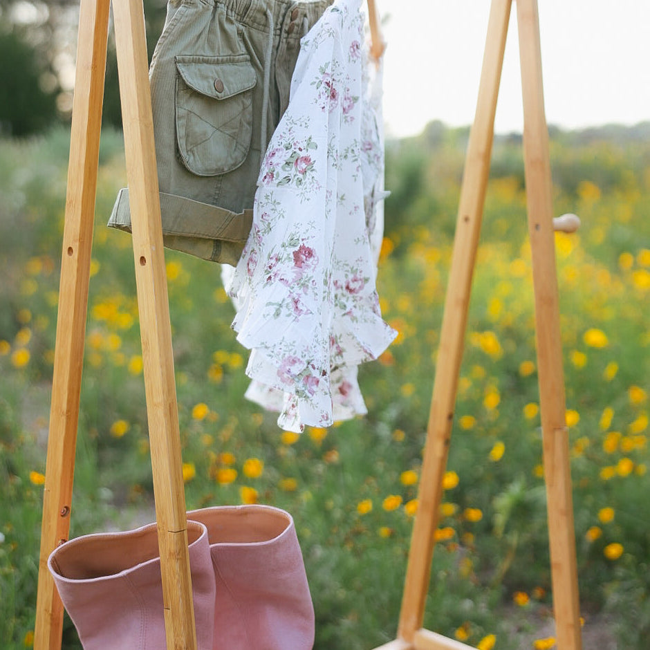 Wooden rack with shorts, a floral dress, and pink boots against a natural background